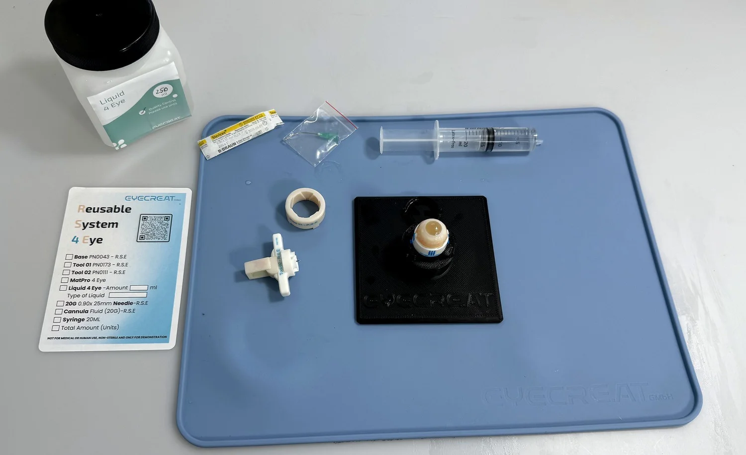 Reusable System 4 Eye set up on a MatPro 4 Eye: assembly station with an assembled eye, Tool 01, Tool 02, syringe, needle and Liquid 4 Eye