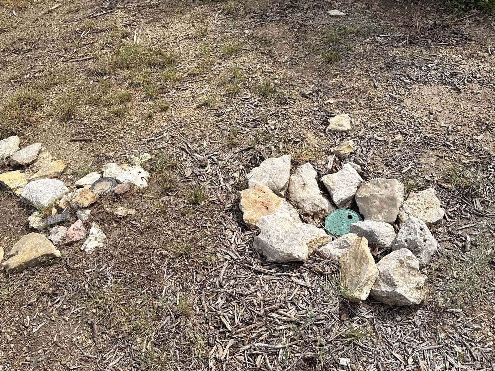 Low point drain for a rainwater collection line, a green round valve box set in the ground among landscaping rock
