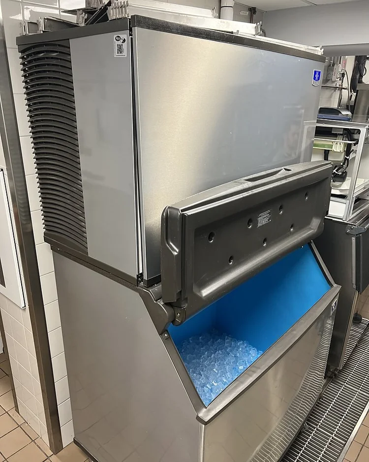 Commercial ice machine over a storage bin in a restaurant kitchen, back in service with clean ice