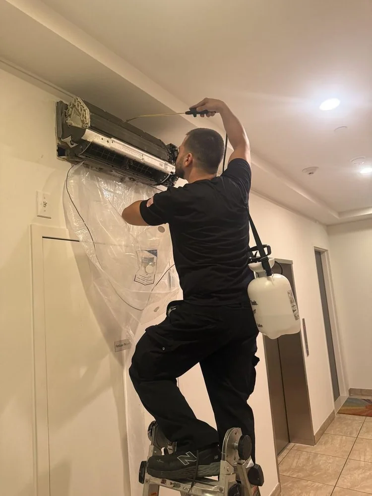 JLL Mechanical technician cleaning a hallway ductless unit with a coil cleaning bag catching the runoff