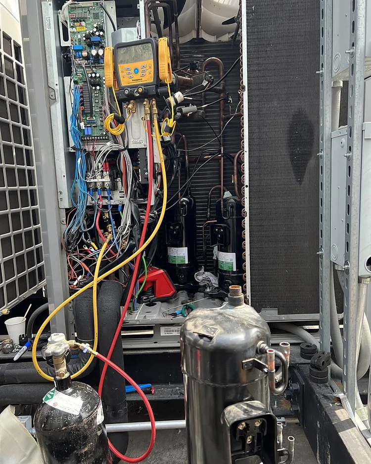 Compressor next to an open VRF outdoor unit on a rooftop platform