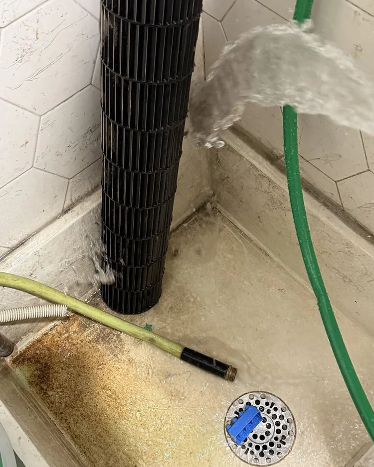 Blower wheel being rinsed with a hose over a drain