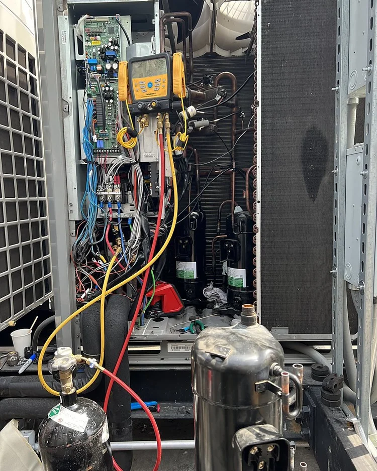 VRF outdoor unit with panels open, a digital manifold gauge set, a nitrogen cylinder and a compressor on the platform
