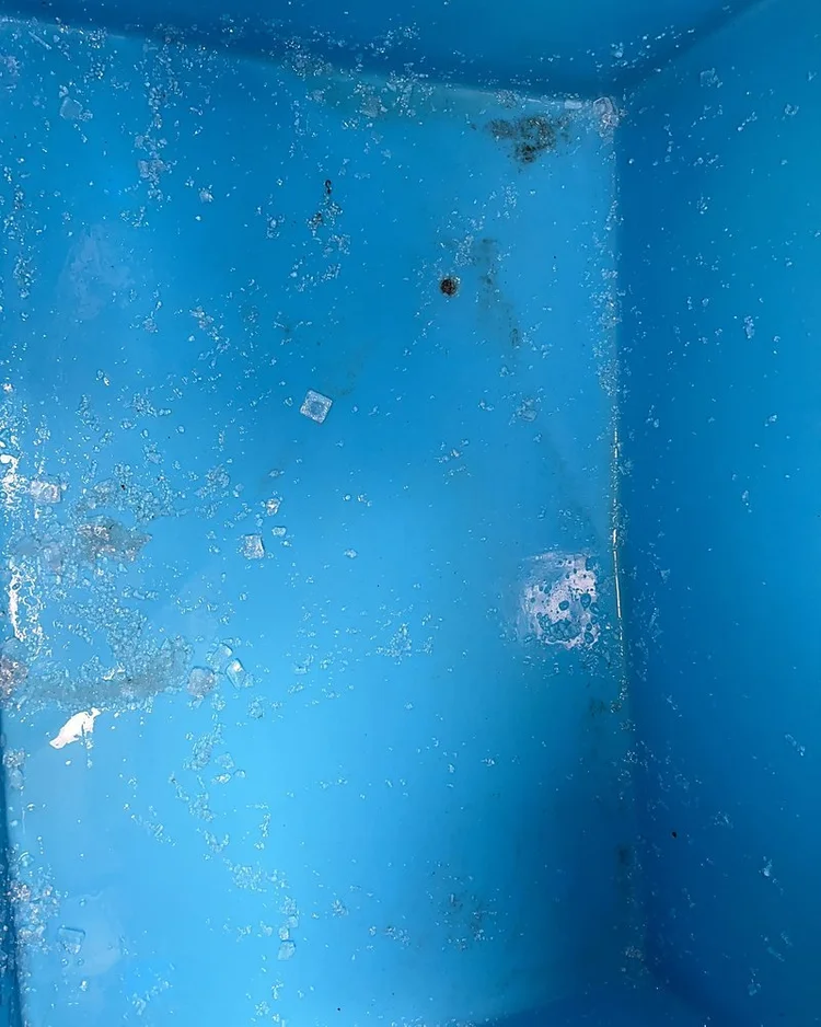 Interior of an ice storage bin with slime and scale stains on the blue liner