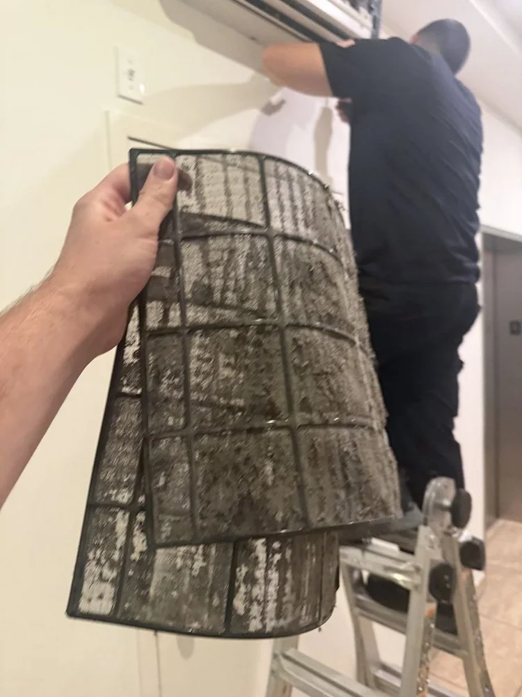 Technician holding a ductless unit air filter fully loaded with dust and lint