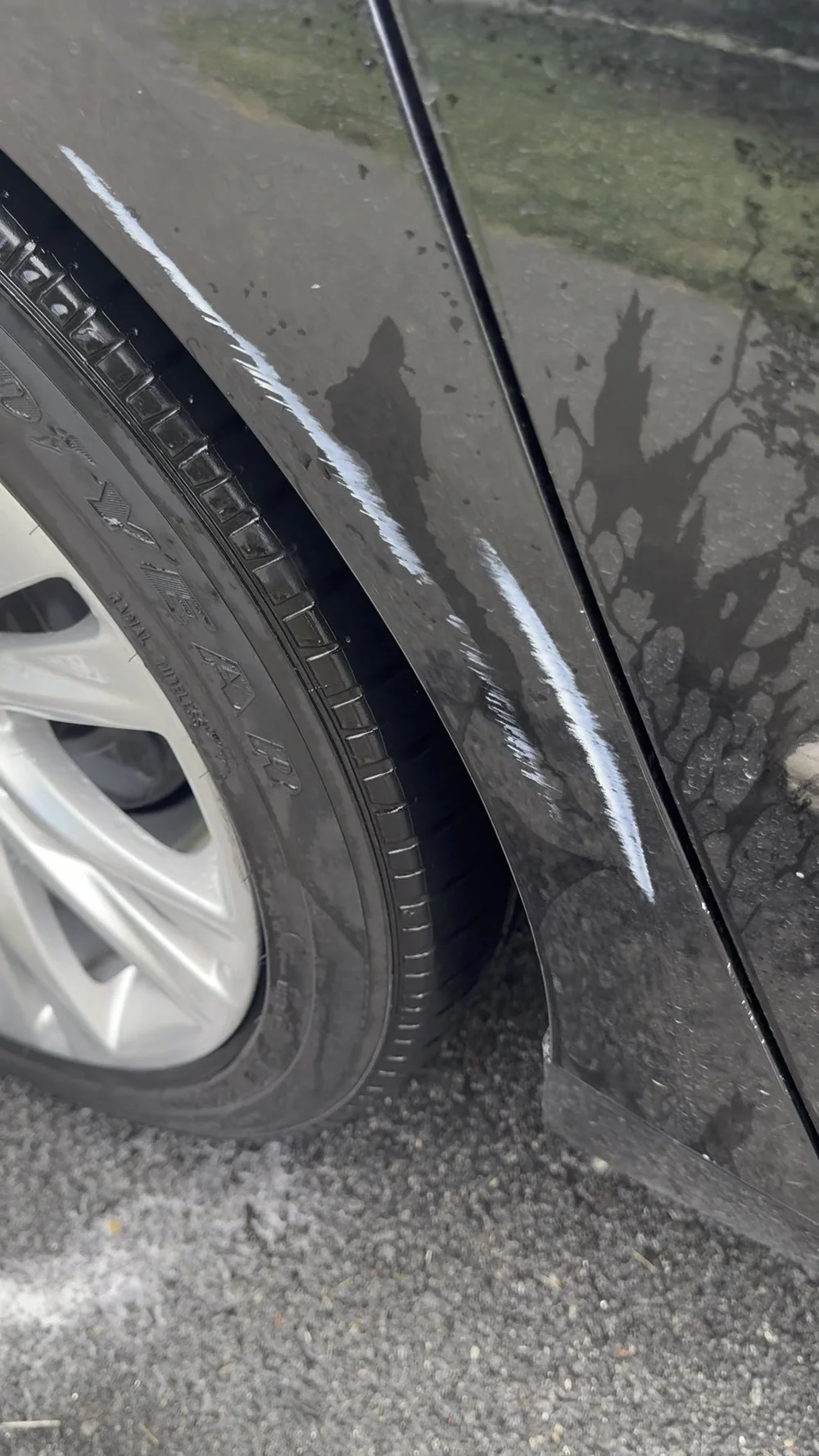 Black vehicle paint before Spot Paint Correction, showing transfer and surface scuffing above the wheel opening.