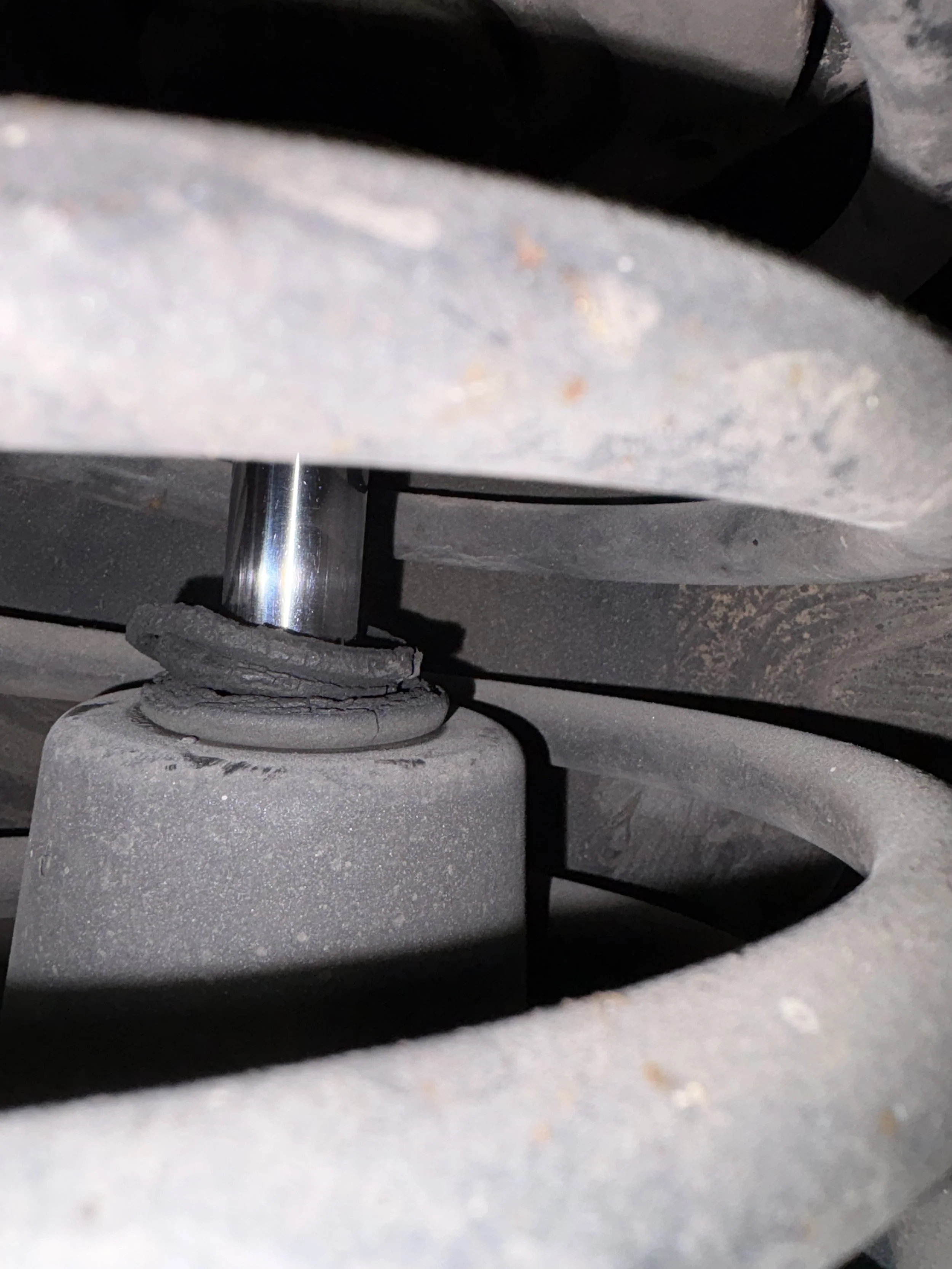 The rear shock absorber bottom mount showing a cracked and deteriorating rubber bushing, shot from inside the spring coils
