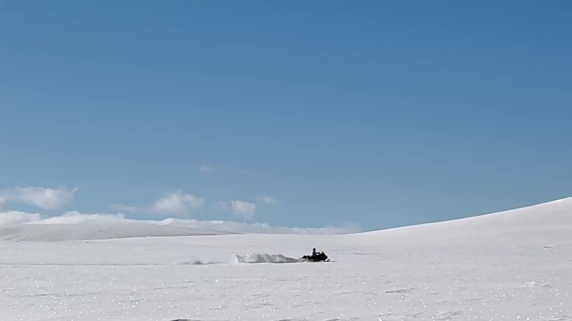 A snowmobile crossing open snow under a blue sky