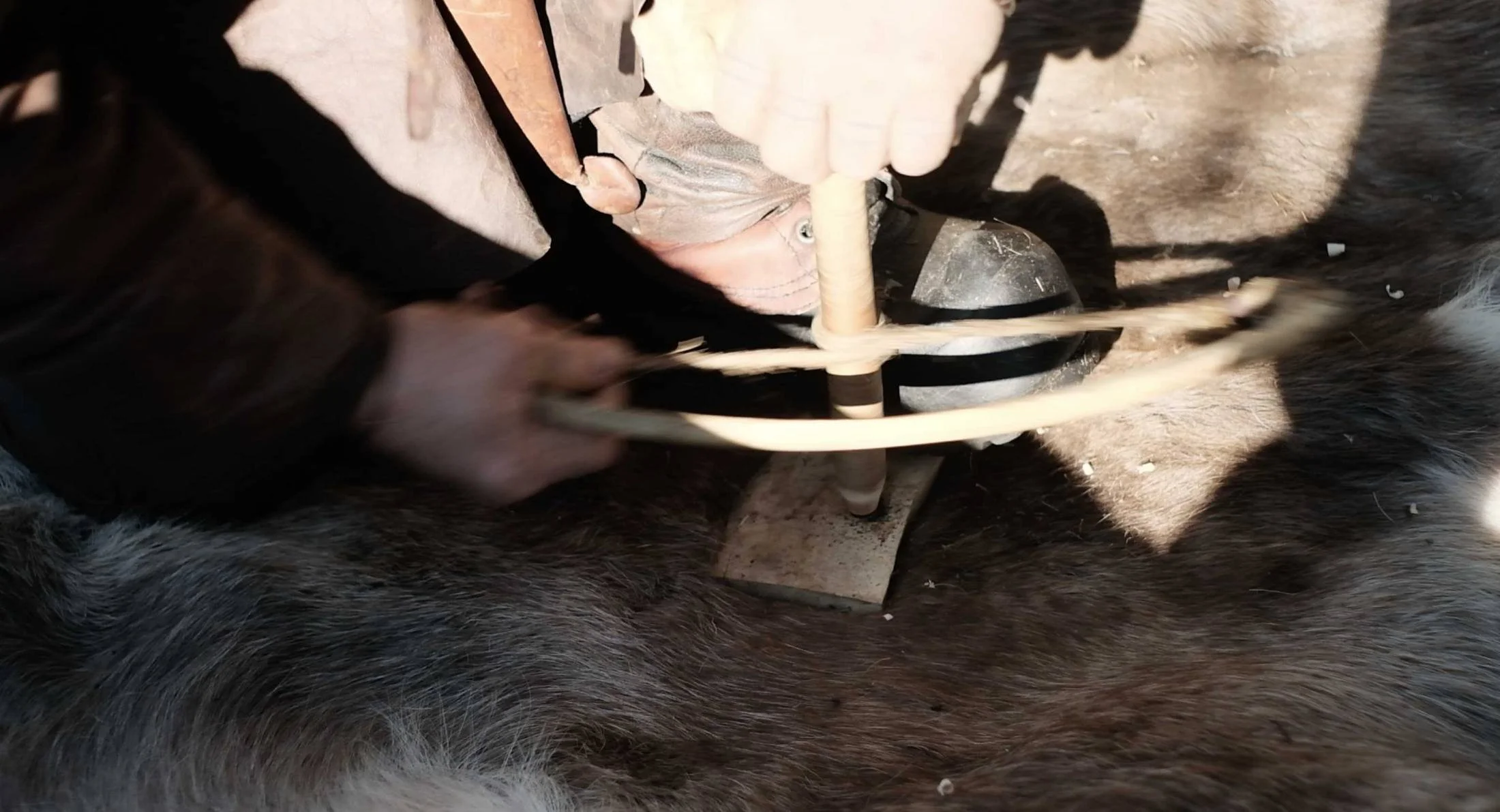 Hands working a bow drill on a reindeer hide