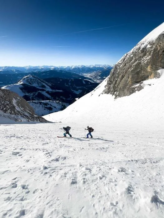 Two skiers crossing a snowfield below a peak