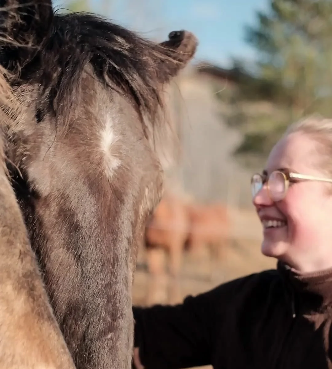 A guest smiling beside a horse's head in the paddock
