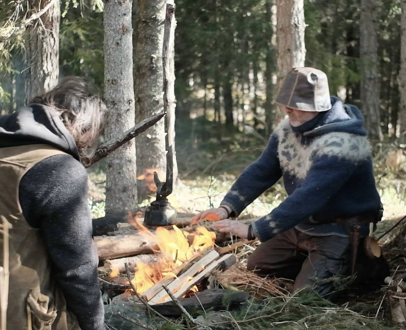 Two people lighting a fire between pine trees