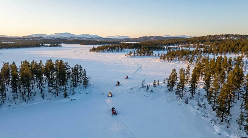 Snowmobiles crossing a frozen lake at dusk