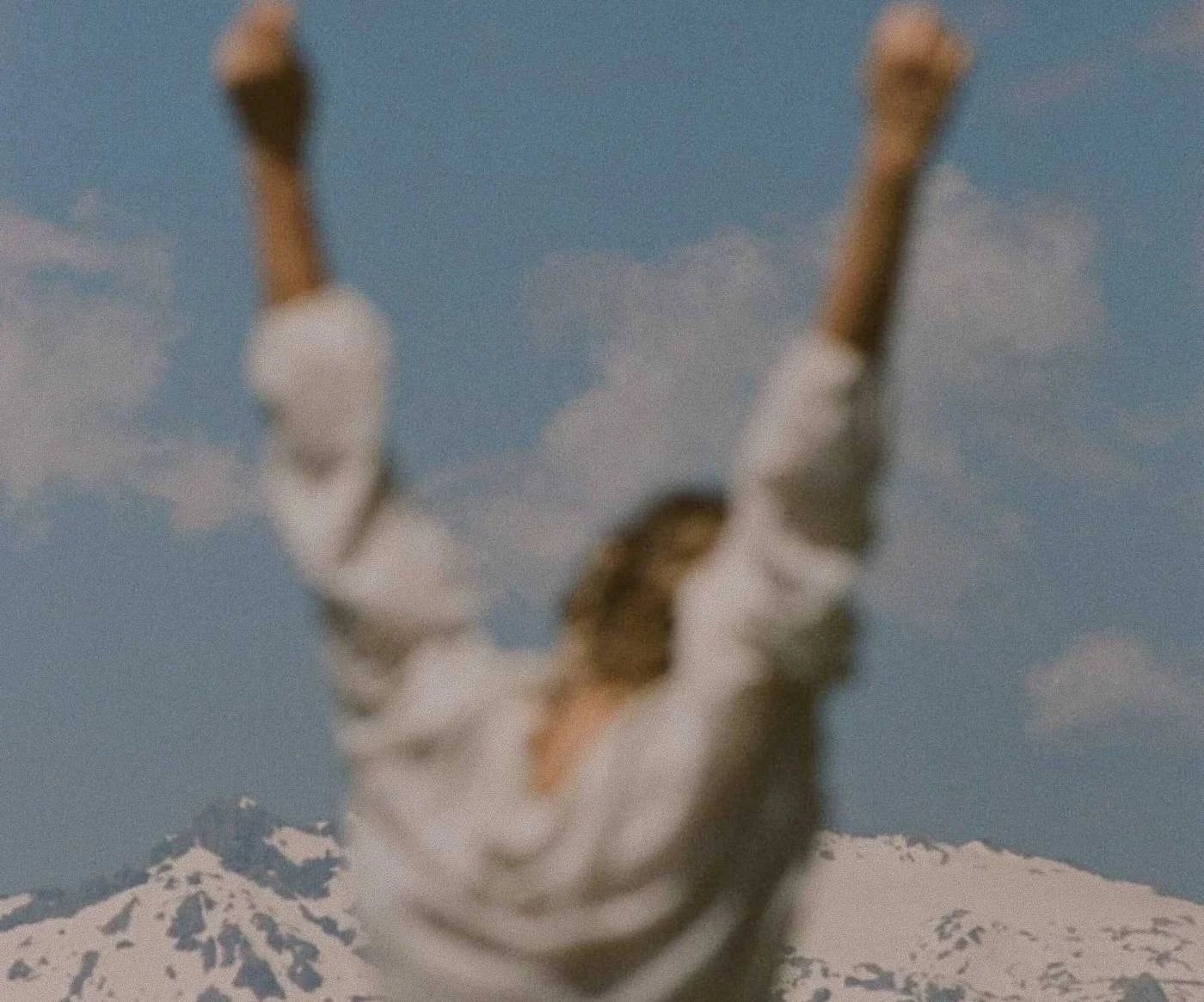 Person with arms raised in front of snowy peaks
