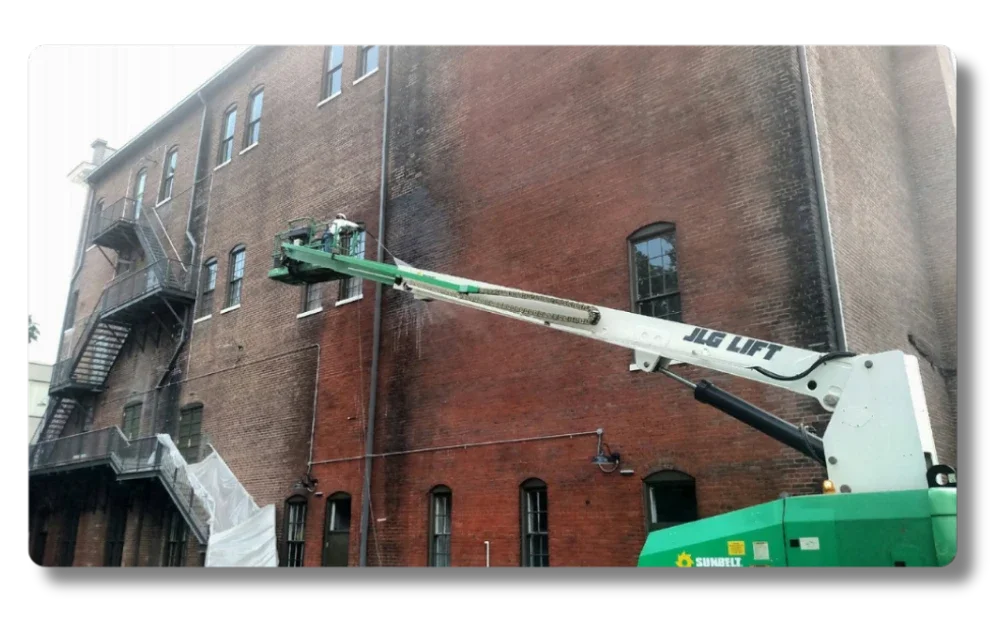 Hot Shot Pressure Washing technician on a JLG boom lift cleaning a multi-story brick building in the Roanoke Valley