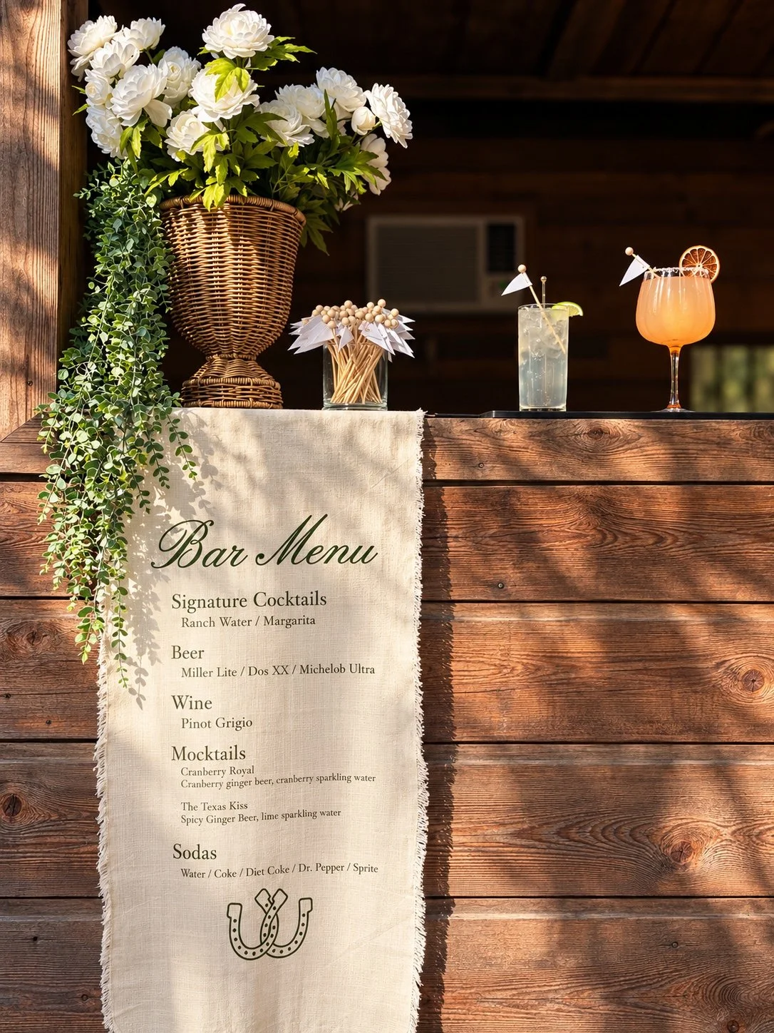Rustic wooden wedding bar with white flowers, signature drinks and a hanging bar menu
