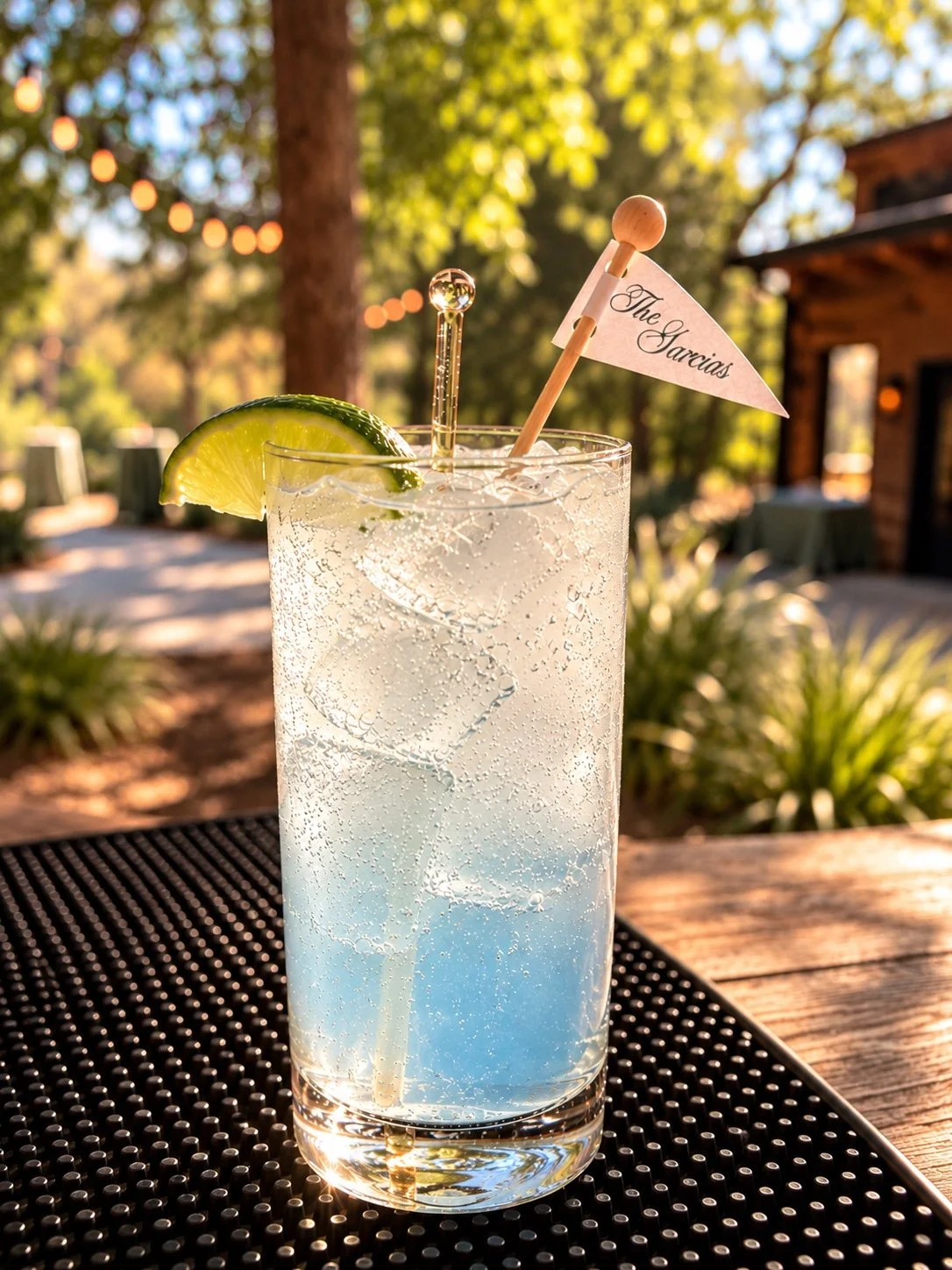 Iced wedding drink with a lime wedge and personalized flag on an outdoor wooden bar