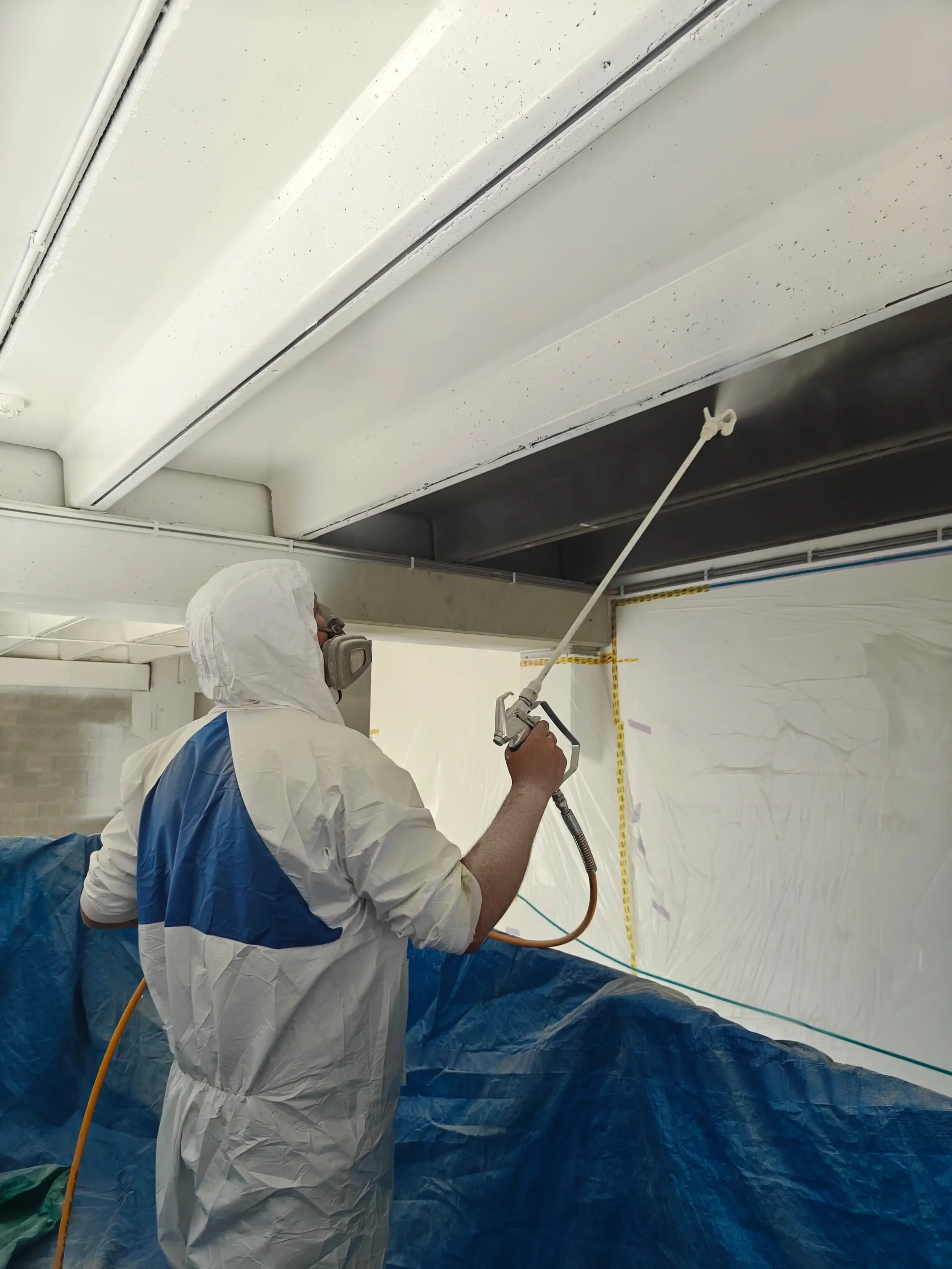 Professionele spuiter met airless pistool bij binnenafwerking industrieel project
