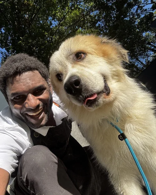 A big fluffy cream dog smiling next to our Lead Groomer