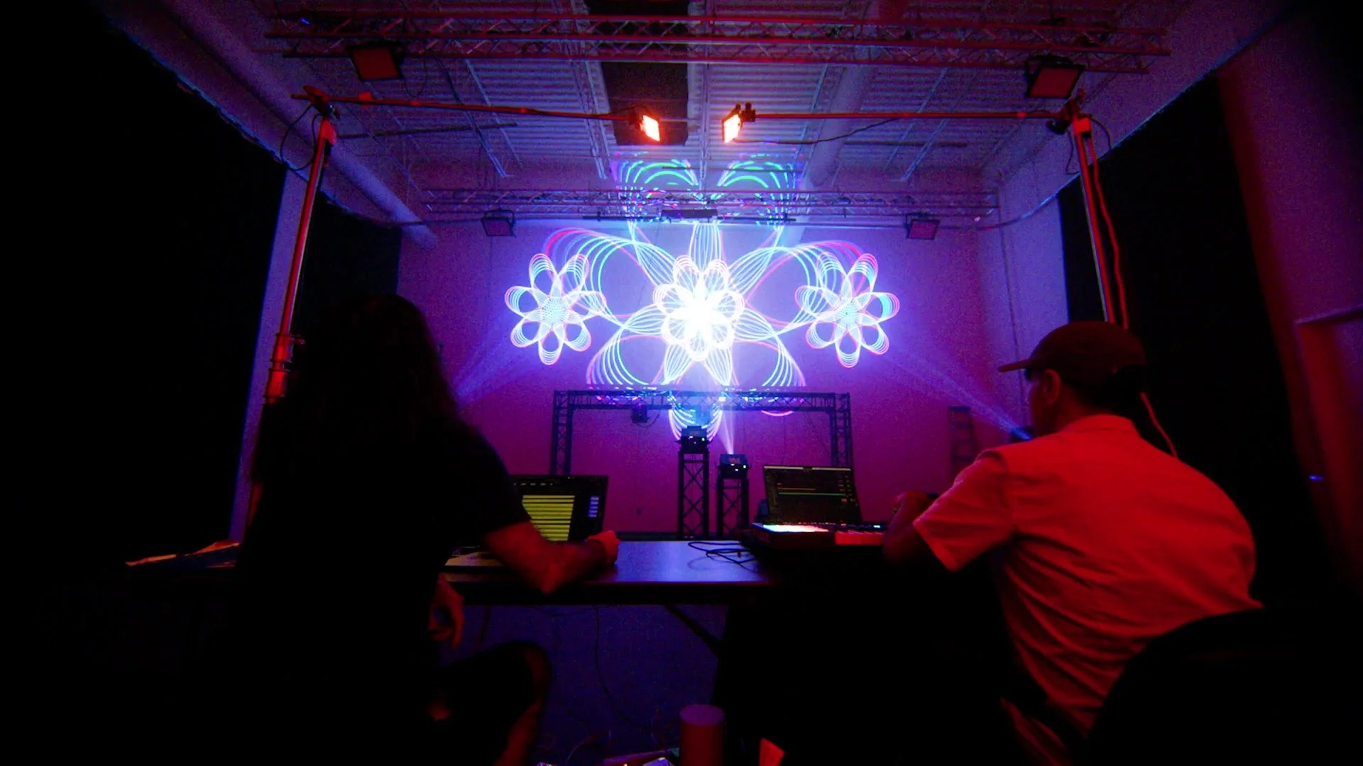 Ramtin Arablouei and Zak Forrest seen from behind, facing colorful laser projections while creating ANIMALCULE