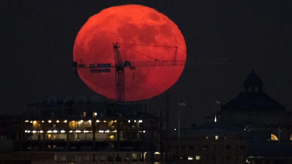 A large orange Moon low above a city skyline.
