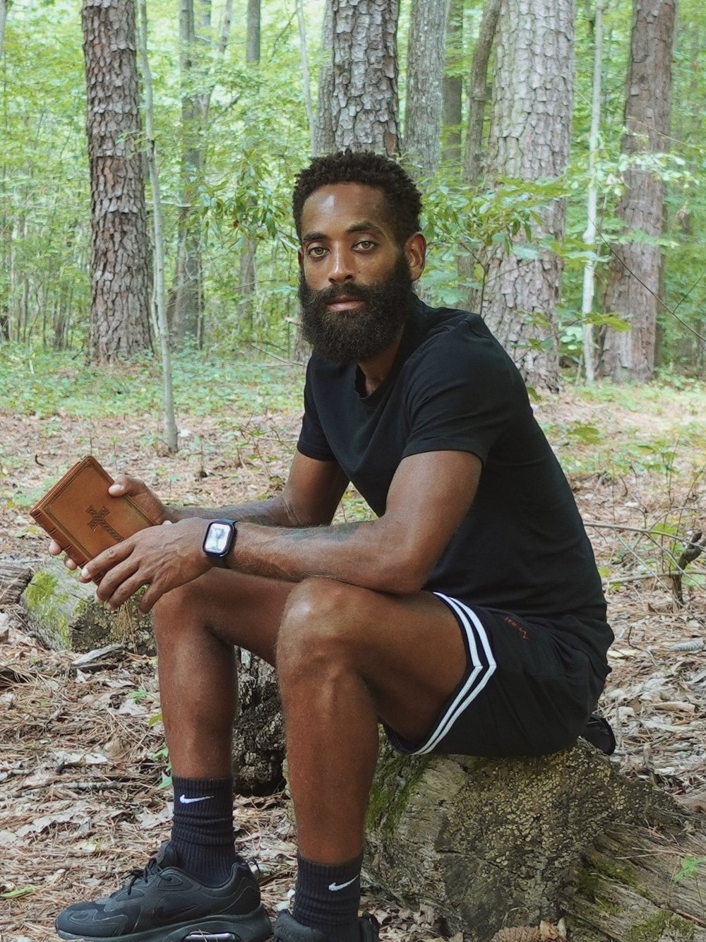 Rashad Houston seated in the woods holding a book.