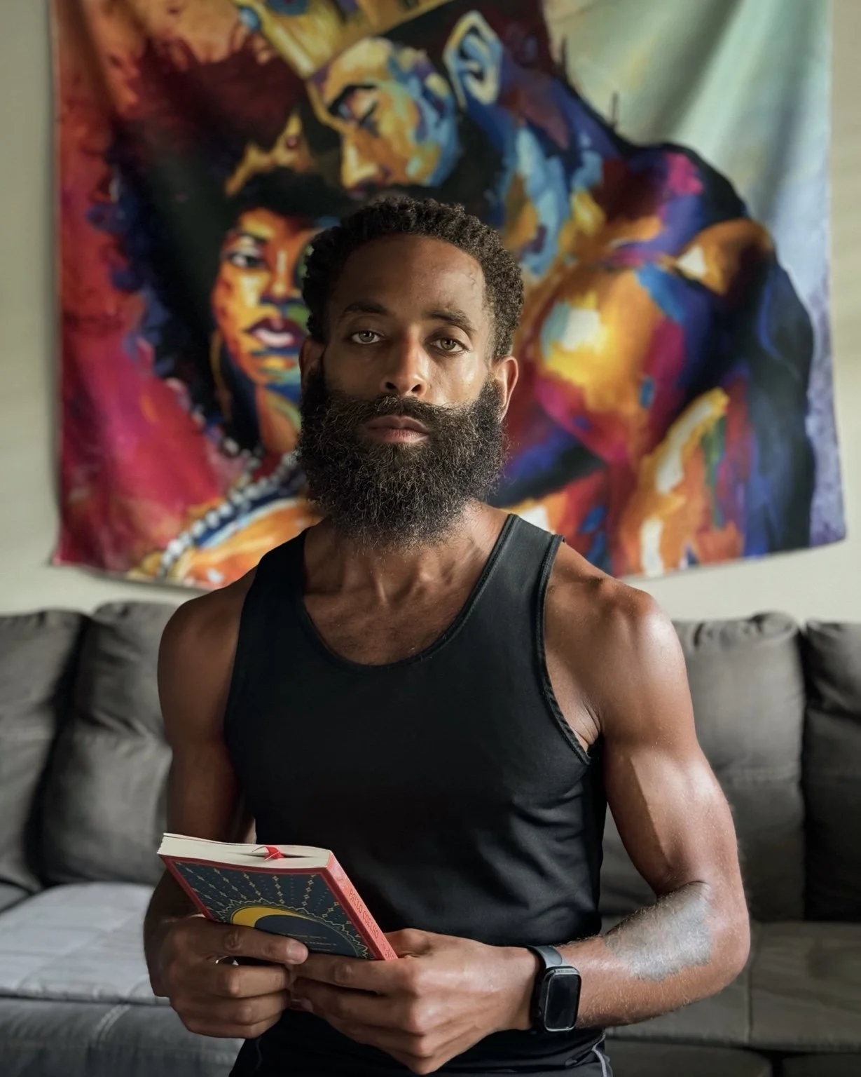 Rashad Houston seated holding a book, with colorful artwork behind him.