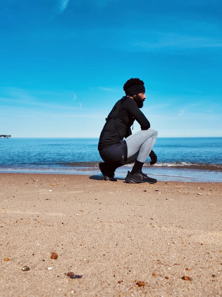 Rashad Houston crouches beside the bay in outdoor training clothes beneath a clear blue sky.