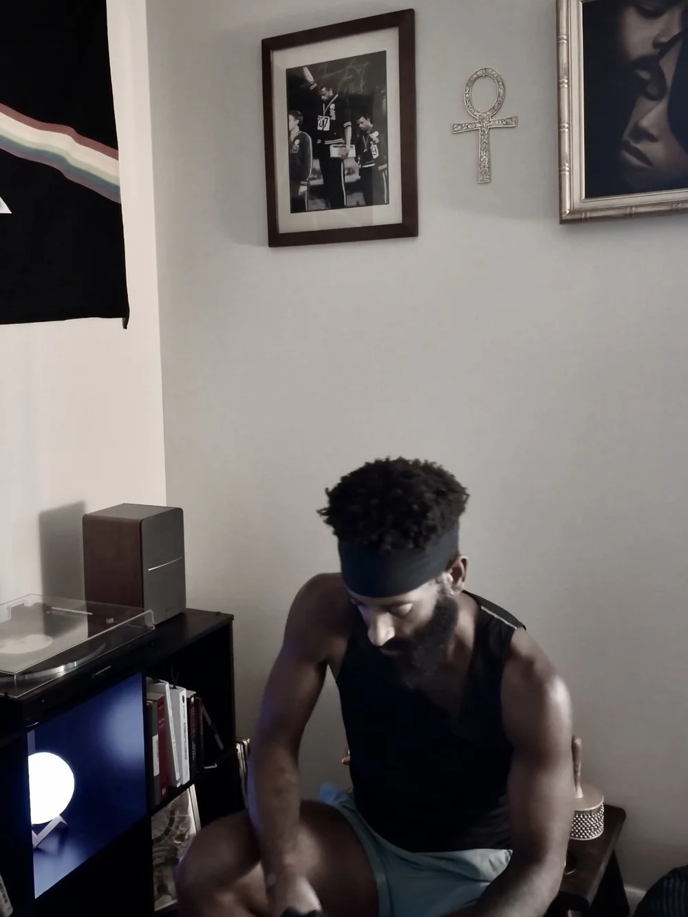 Rashad seated at home in a black tank top, headband, and running shorts.