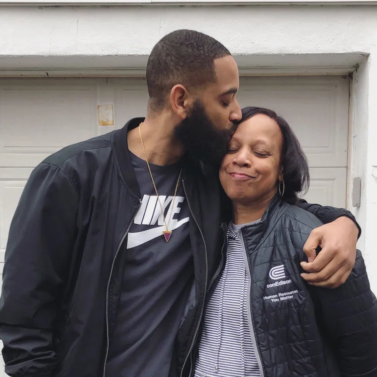 Rashad embracing a woman and kissing her forehead outside a home.
