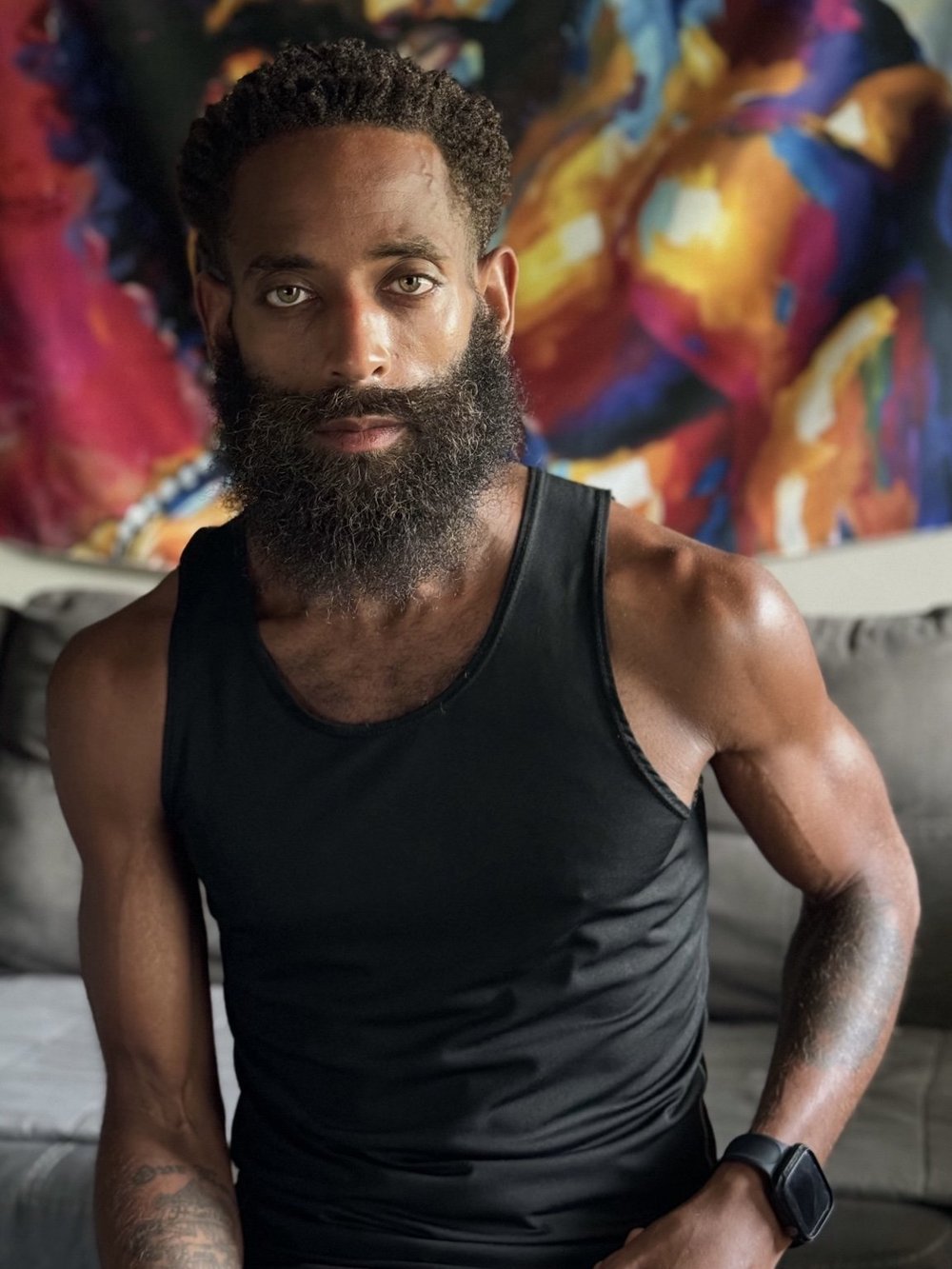Portrait of Rashad Houston seated in a black tank top, with colorful abstract artwork behind him.