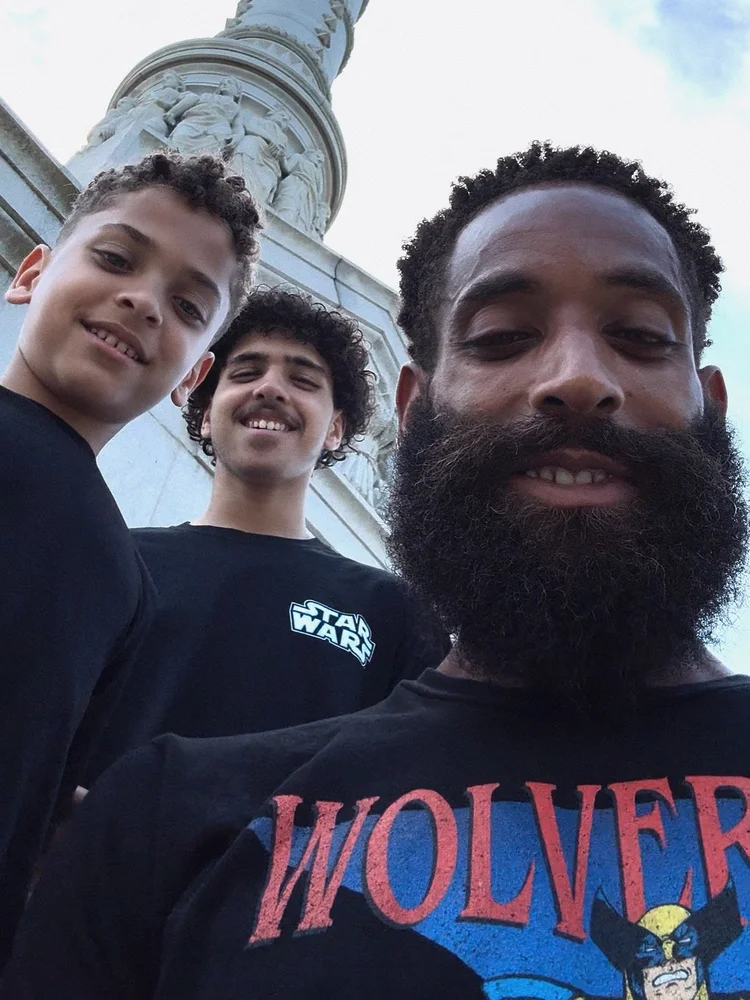 Rashad and his sons Aidan and Omari smiling together in a second outdoor selfie.