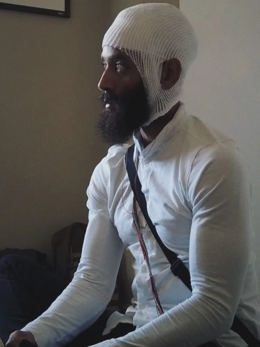 Rashad Houston seated at home wearing a gauze head covering and EEG monitoring wires.