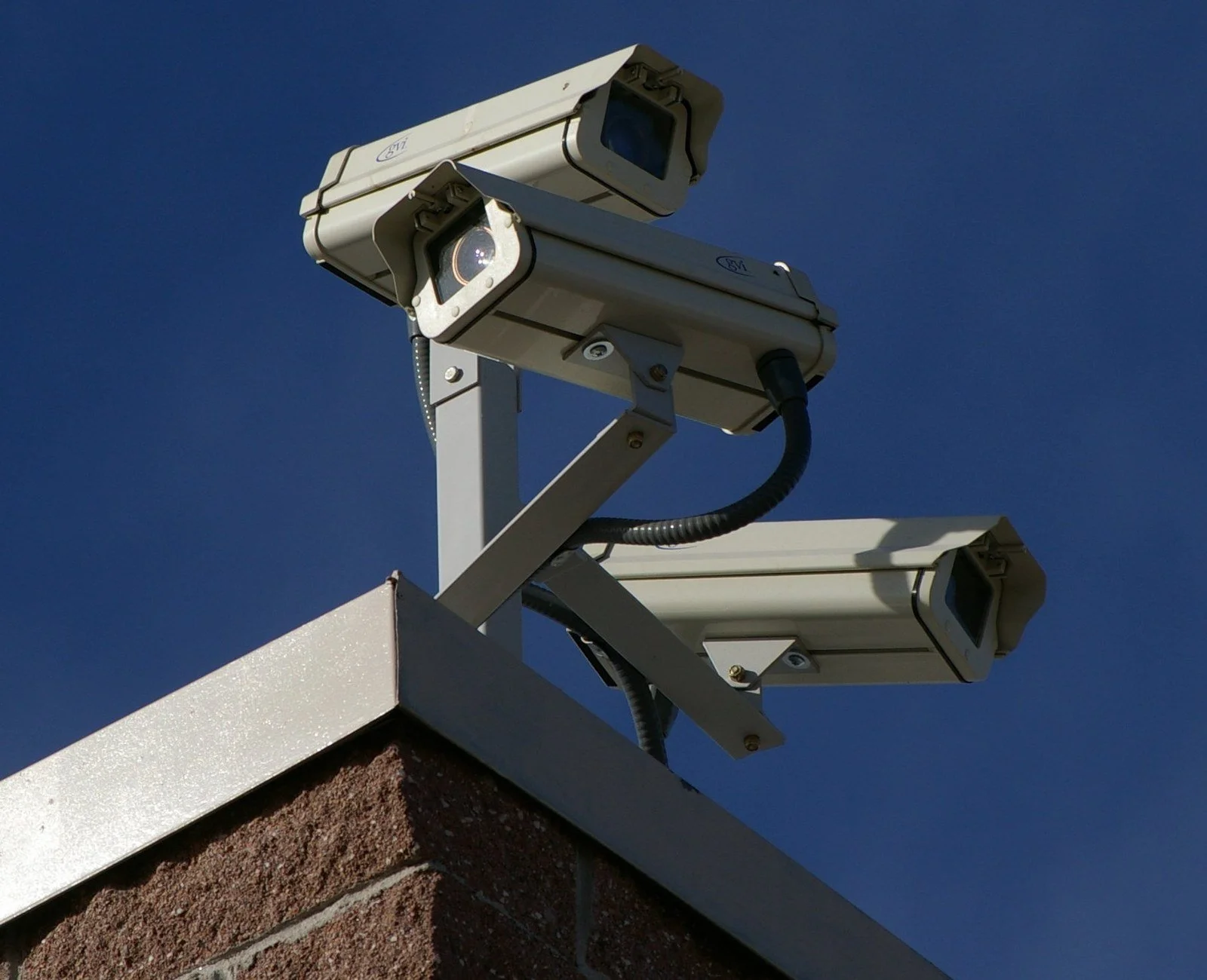 Three surveillance cameras mounted above the corner of a brick building, pointing in different directions.