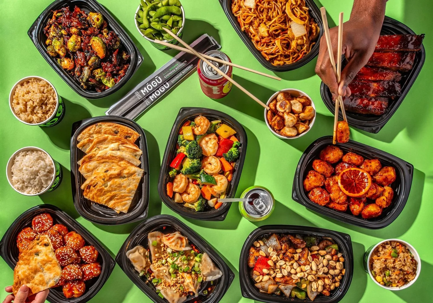 A full MÓGŪ spread of orange chicken, dumplings, noodles, and rice