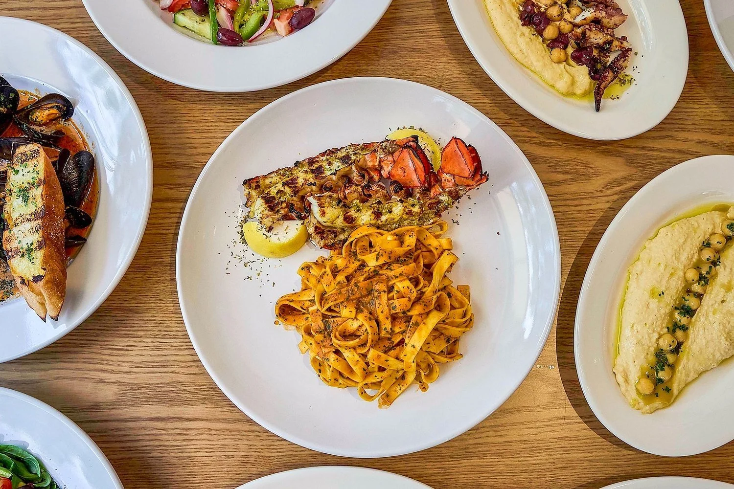 A spread of dishes: grilled lobster tail with tagliatelle, mussels, hummus, octopus and salad