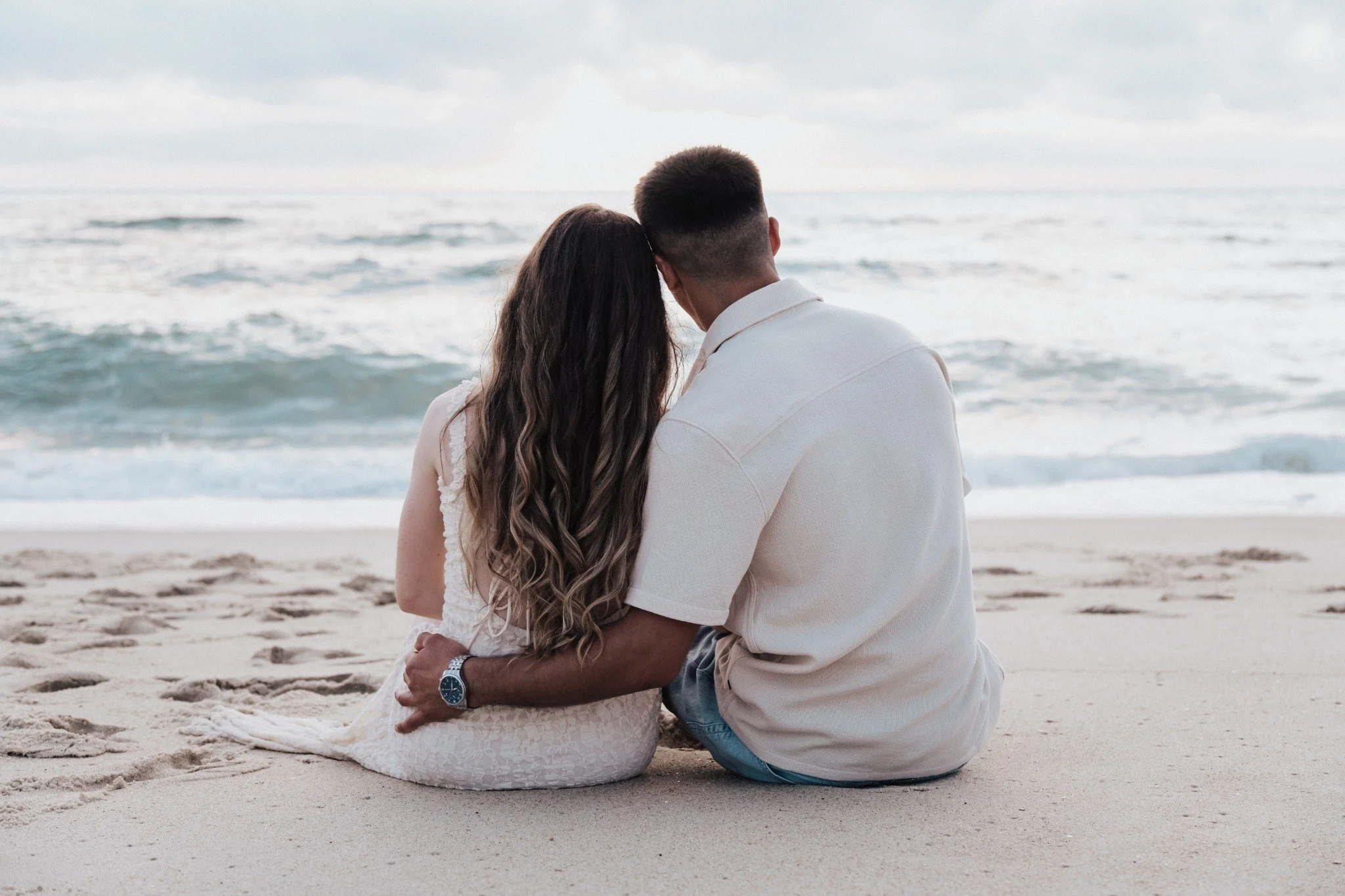 Casal sentado na areia a olhar para o mar