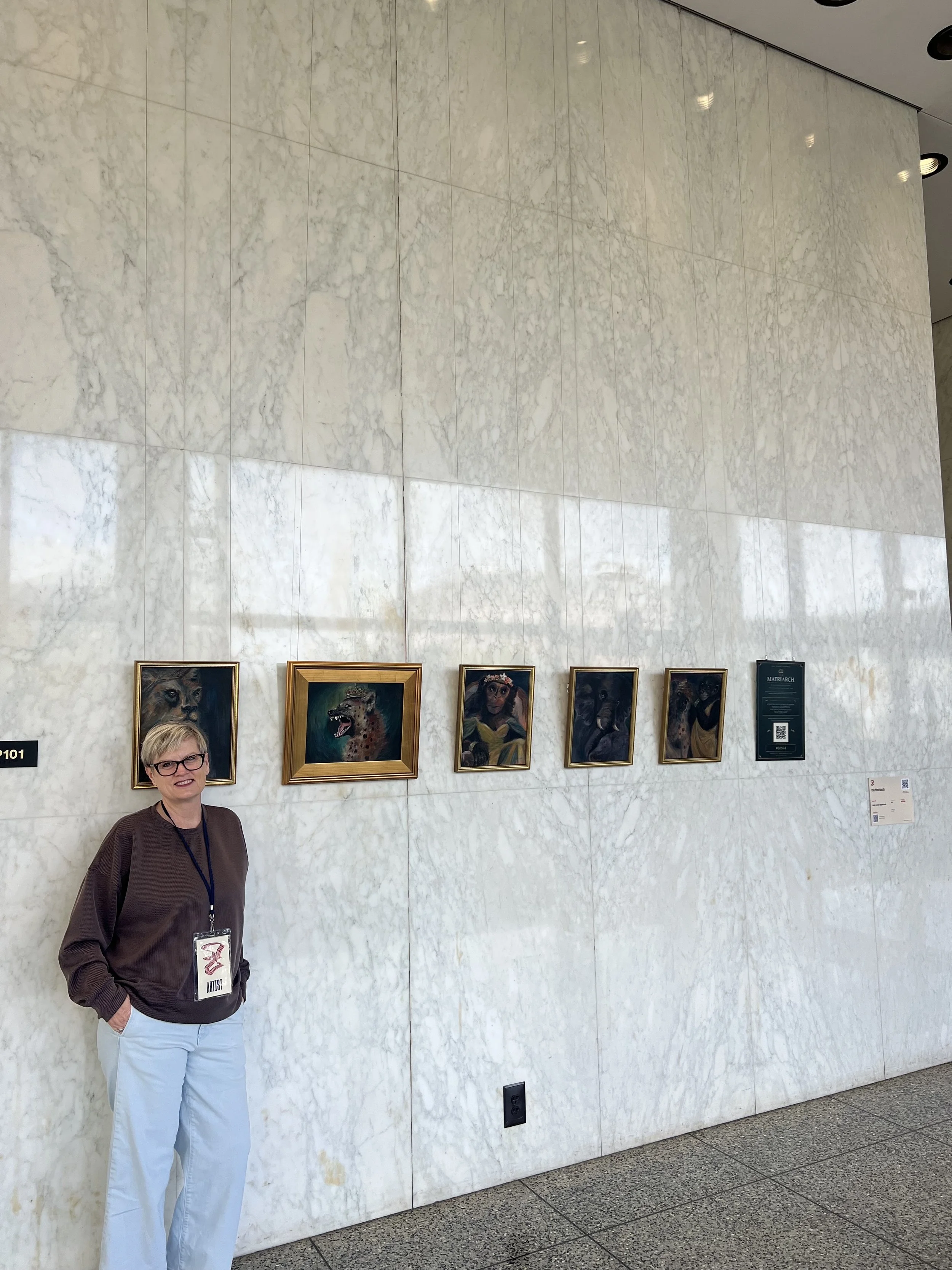 Kelly Lynne Figueiredo standing beside all five paintings from The Matriarch installed at Grand Rapids City Hall during ArtPrize 2026.