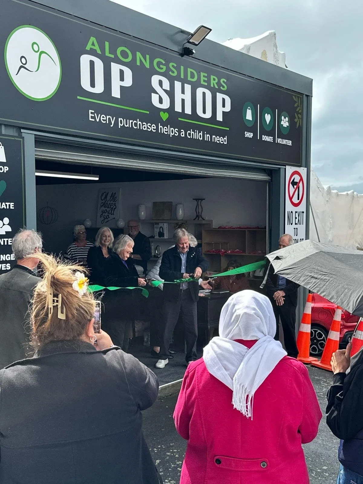 Opening day at the Alongsiders Op Shop: the ribbon is cut outside the shop while a crowd watches.