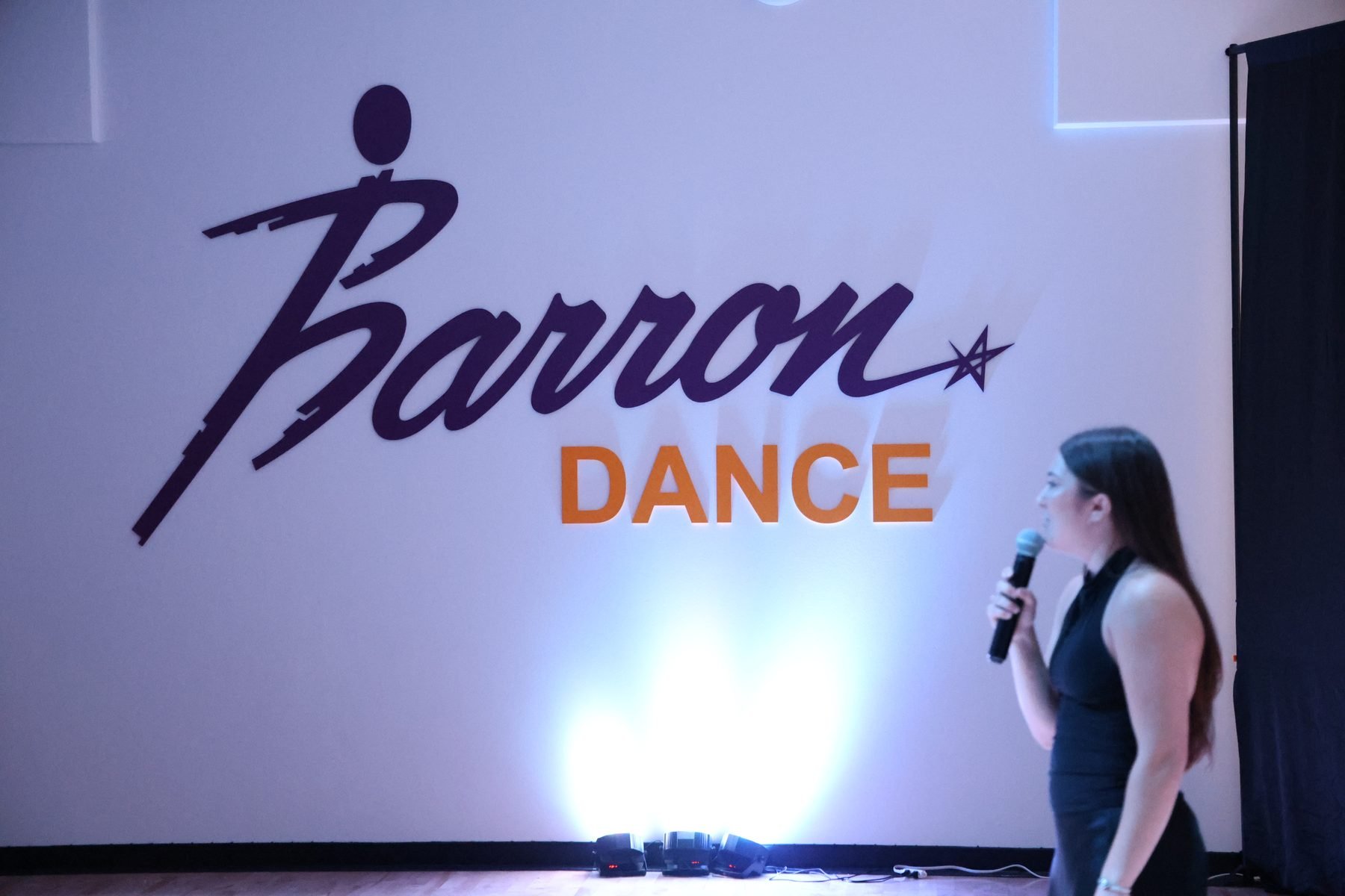 The Barron Dance logo on the studio wall in Ballwin, with an instructor at the microphone