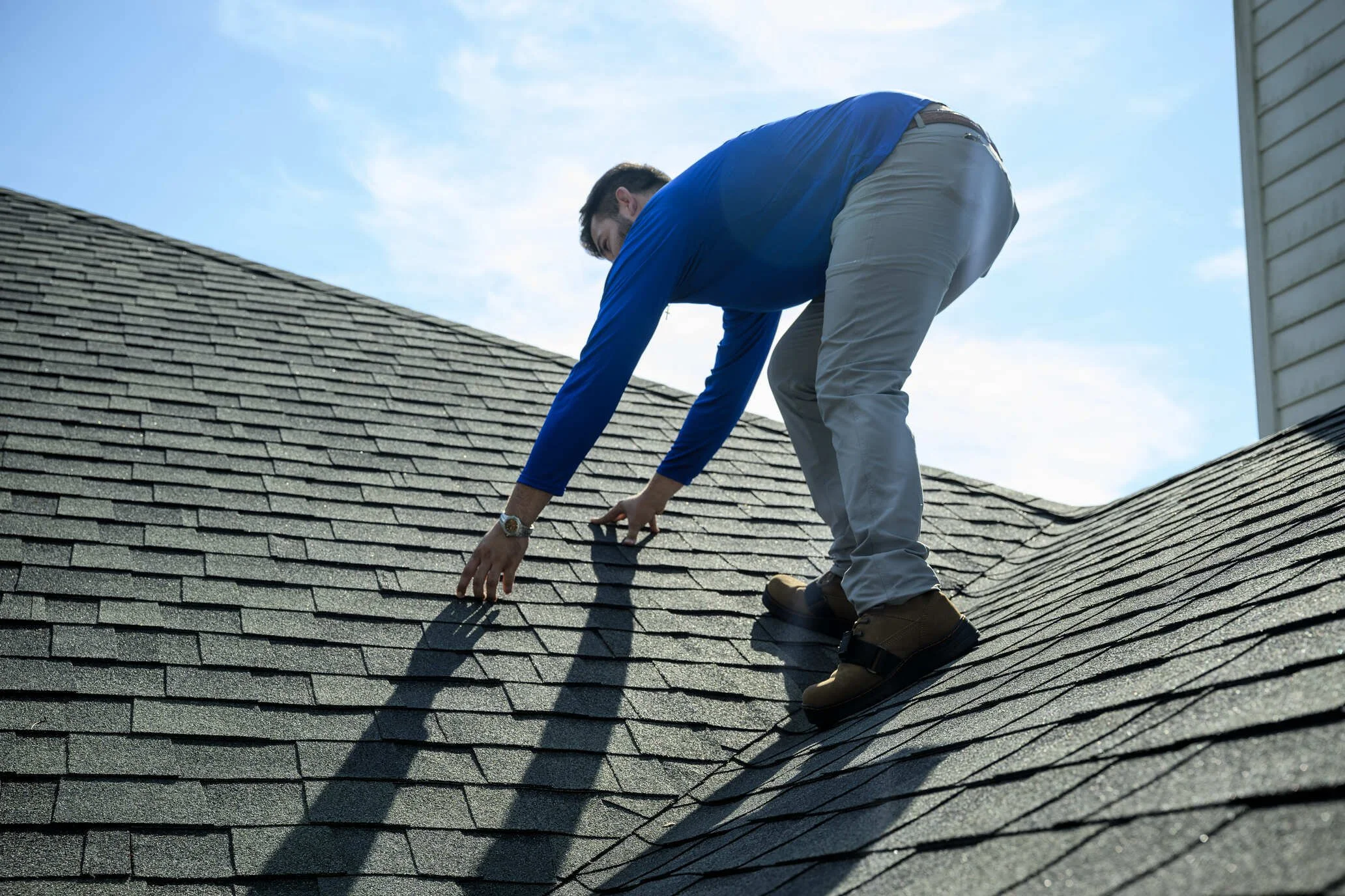 Epic Roofing crew member bending over a dark shingle roof beside a sided wall
