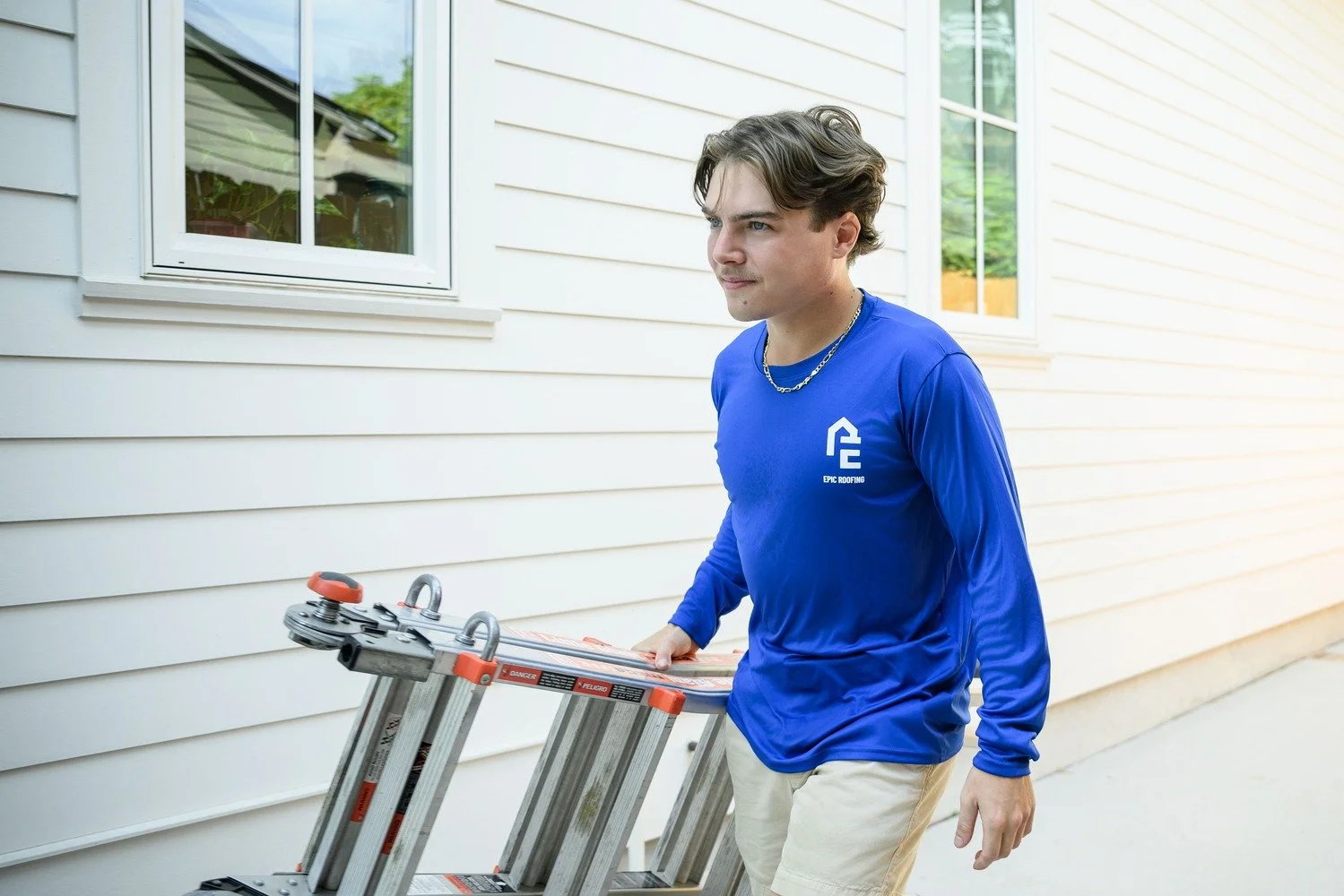 Epic Roofing crew member carrying a ladder along the side of a house