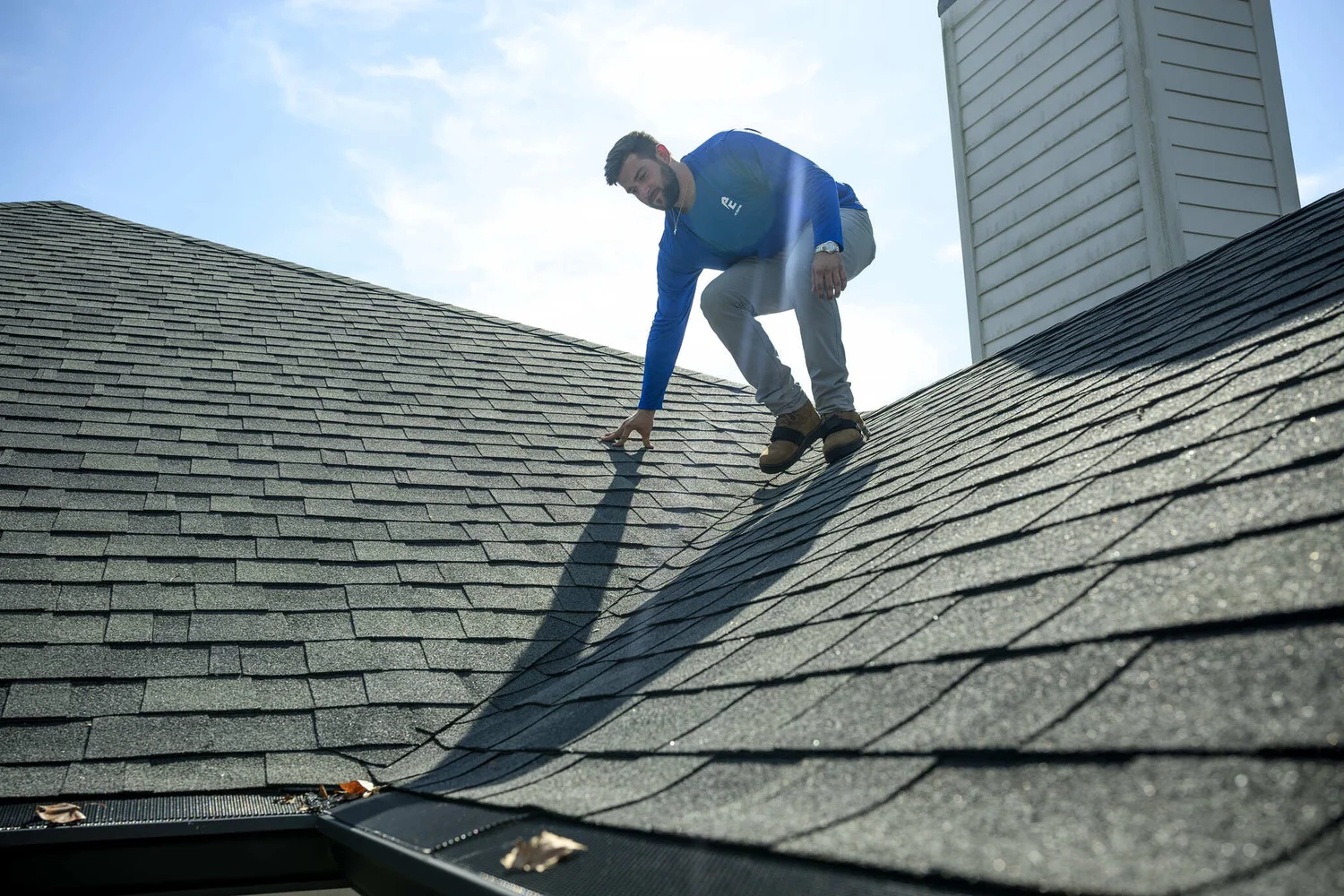 Epic Roofing crew member crouched on a grey architectural-shingle roof beside a chimney