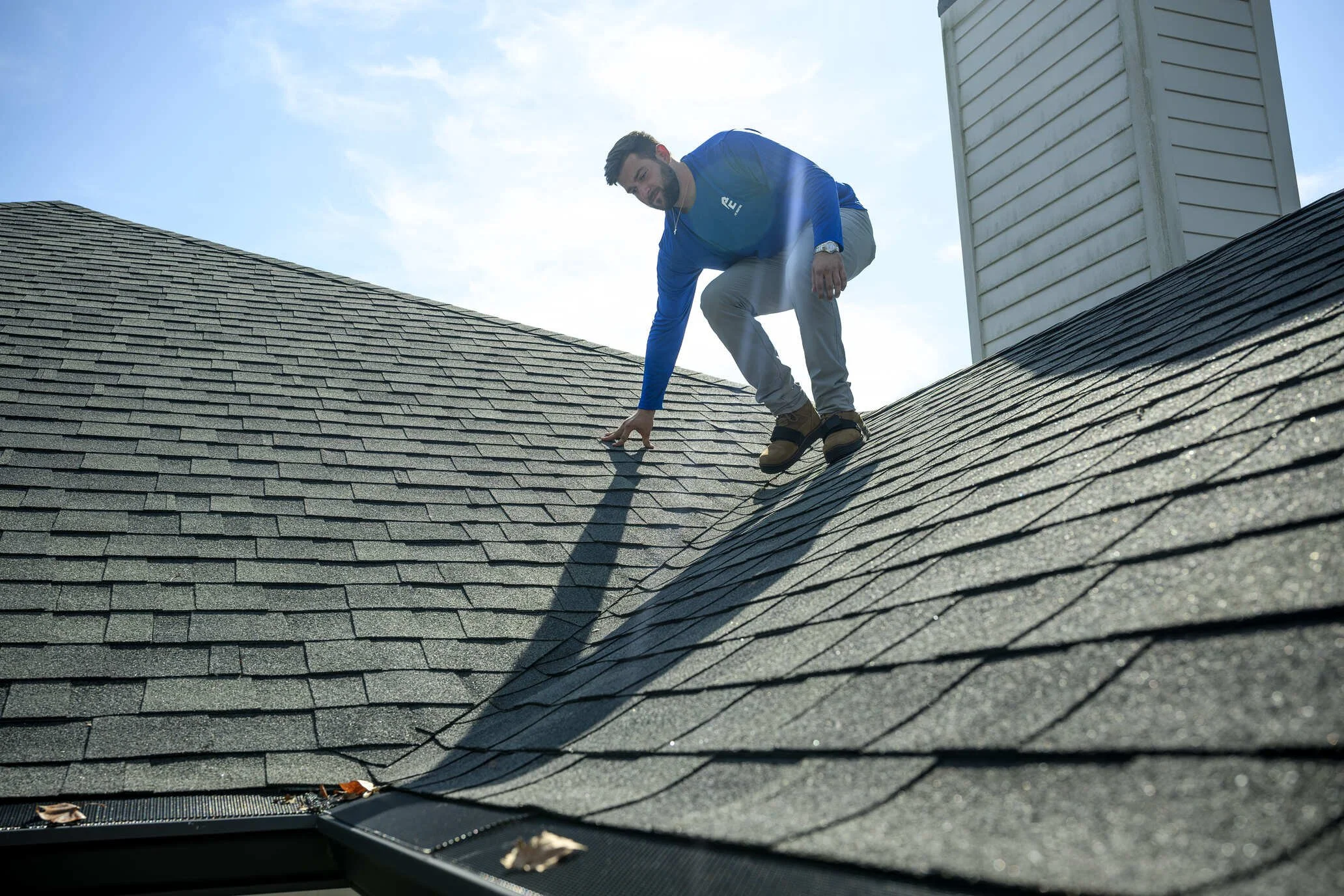 Epic Roofing crew member crouched on a grey architectural-shingle roof beside a chimney