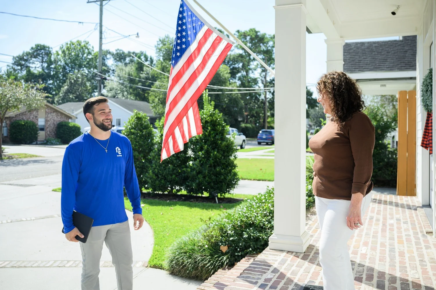Epic Roofing crew member beside a homeowner on a front porch with an American flag