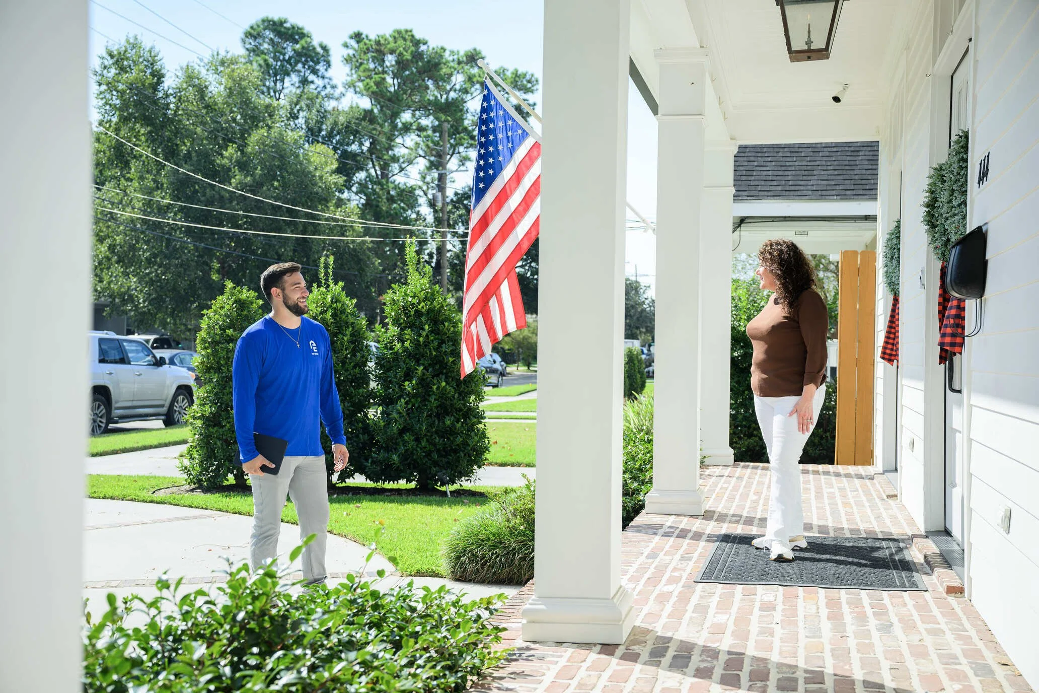 Epic Roofing crew member and a homeowner on a front porch with an American flag