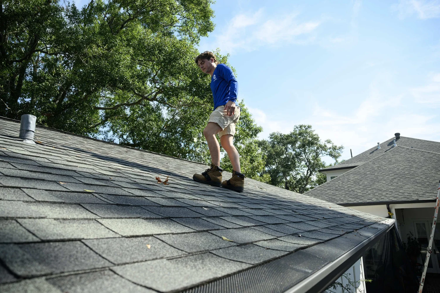 Epic Roofing crew member standing on a grey shingle slope under overhanging trees