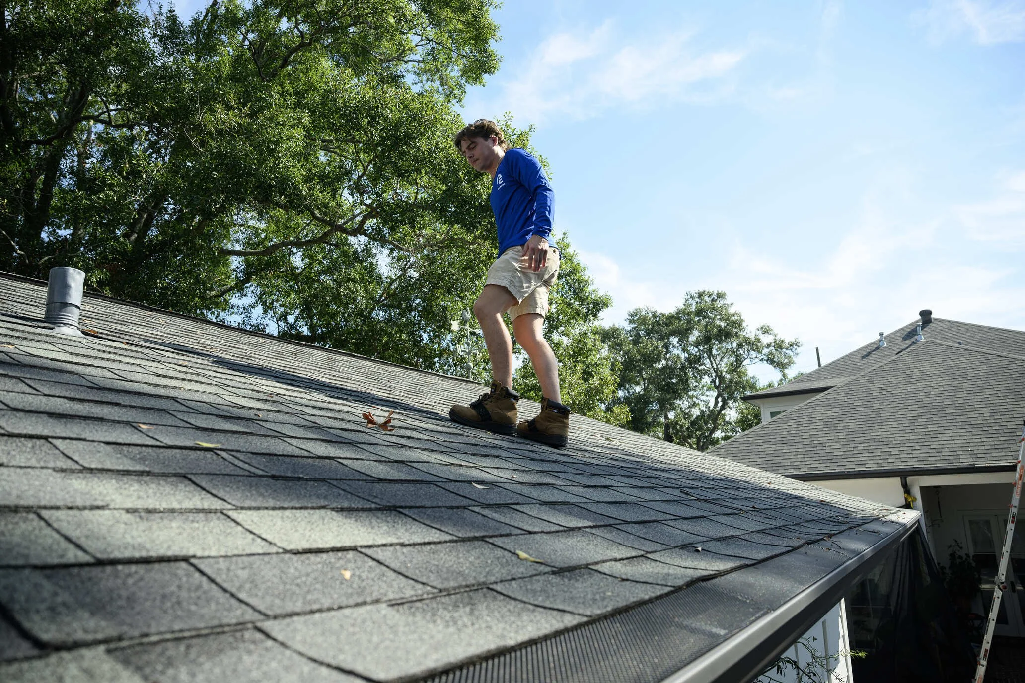 Epic Roofing crew member standing on a grey shingle slope under overhanging trees