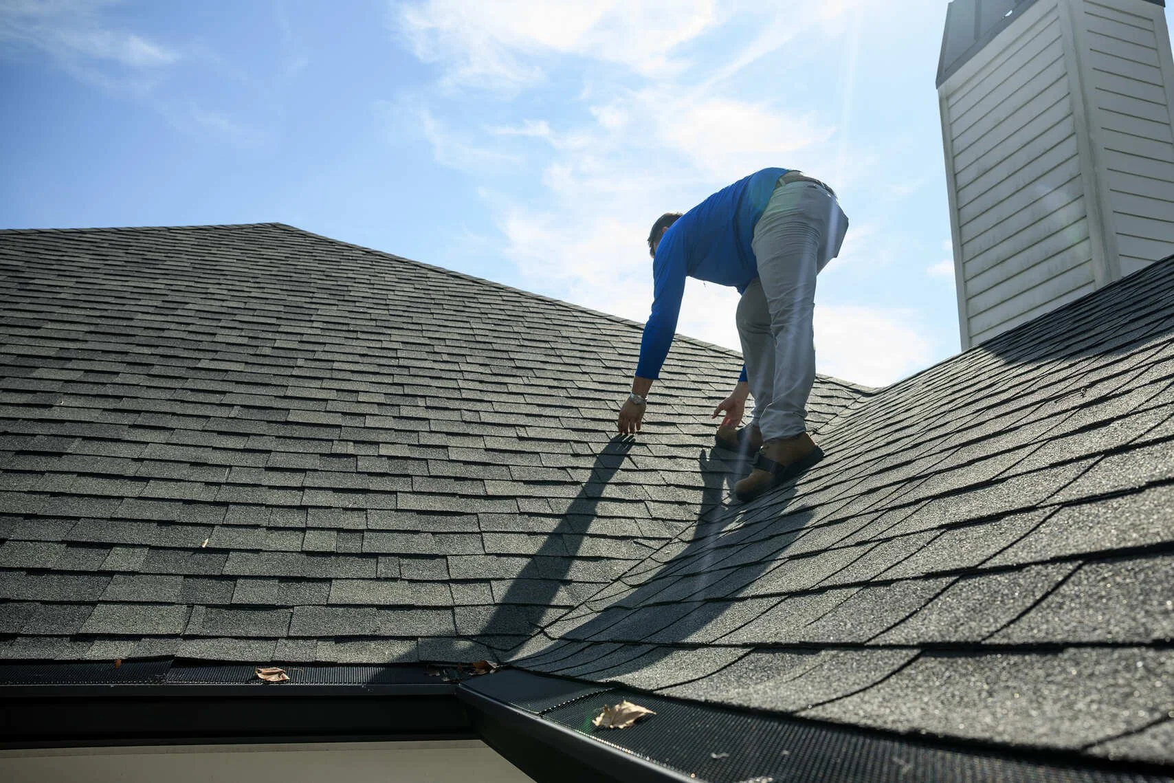 Epic Roofing crew member bending over a grey shingle slope beside a chimney