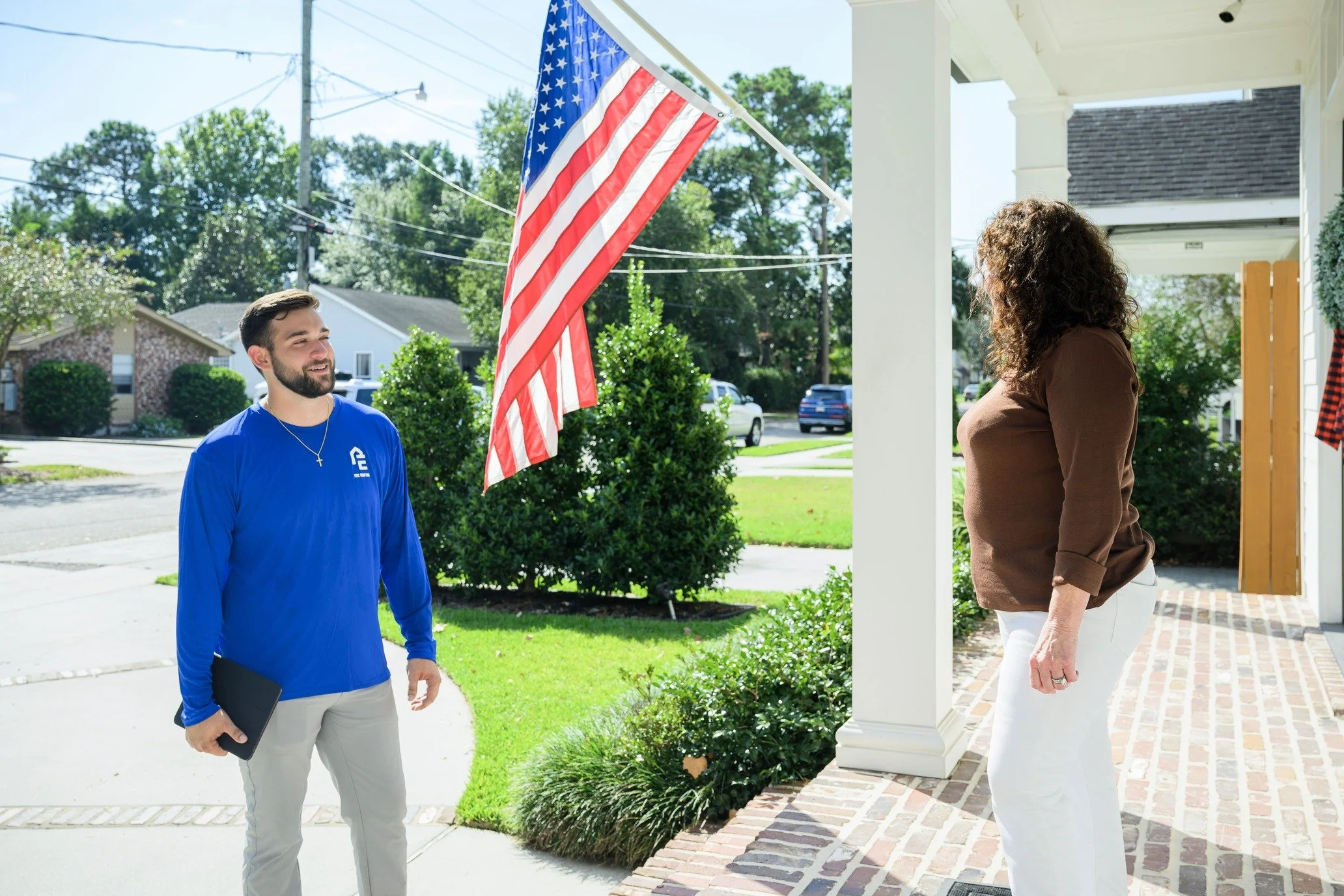 Epic Roofing crew member and a homeowner talking on a front porch with an American flag
